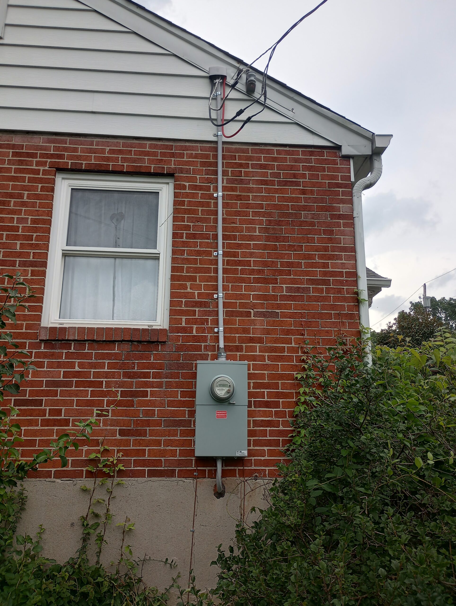 Electric meter with emergency disconnect on a brick wall, conduit running up to the weatherhead