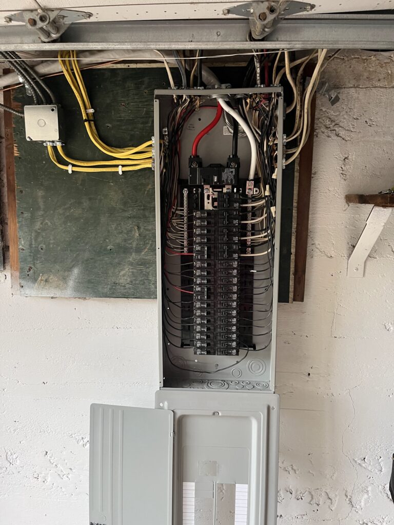 An open 200-amp residential electrical breaker panel mounted on a wall, showing wiring, circuit breakers, and the main disconnect with the cover partially removed.