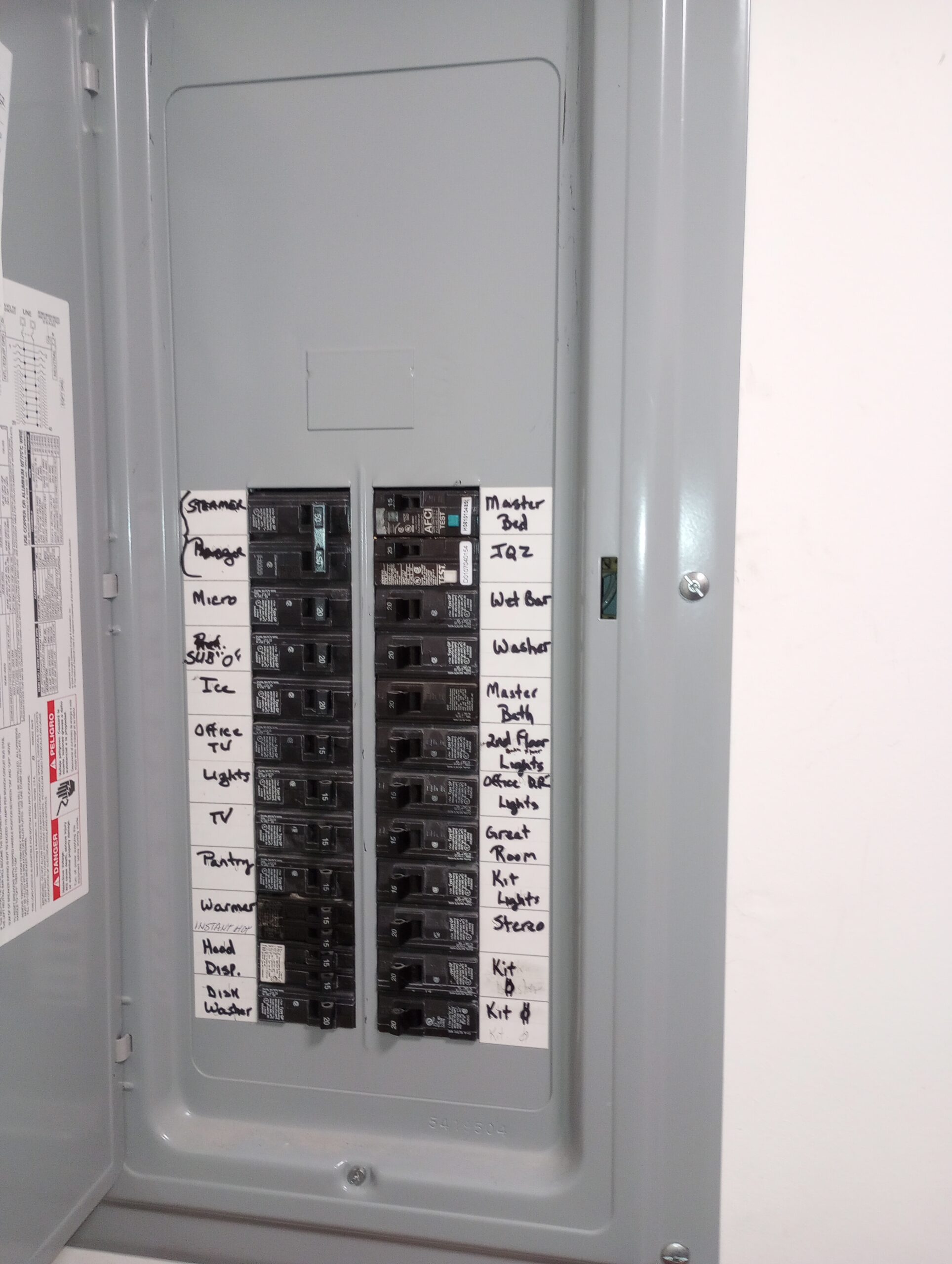 Open residential panel with handwritten labels for circuits including microwave, office, master bedroom and wet bar